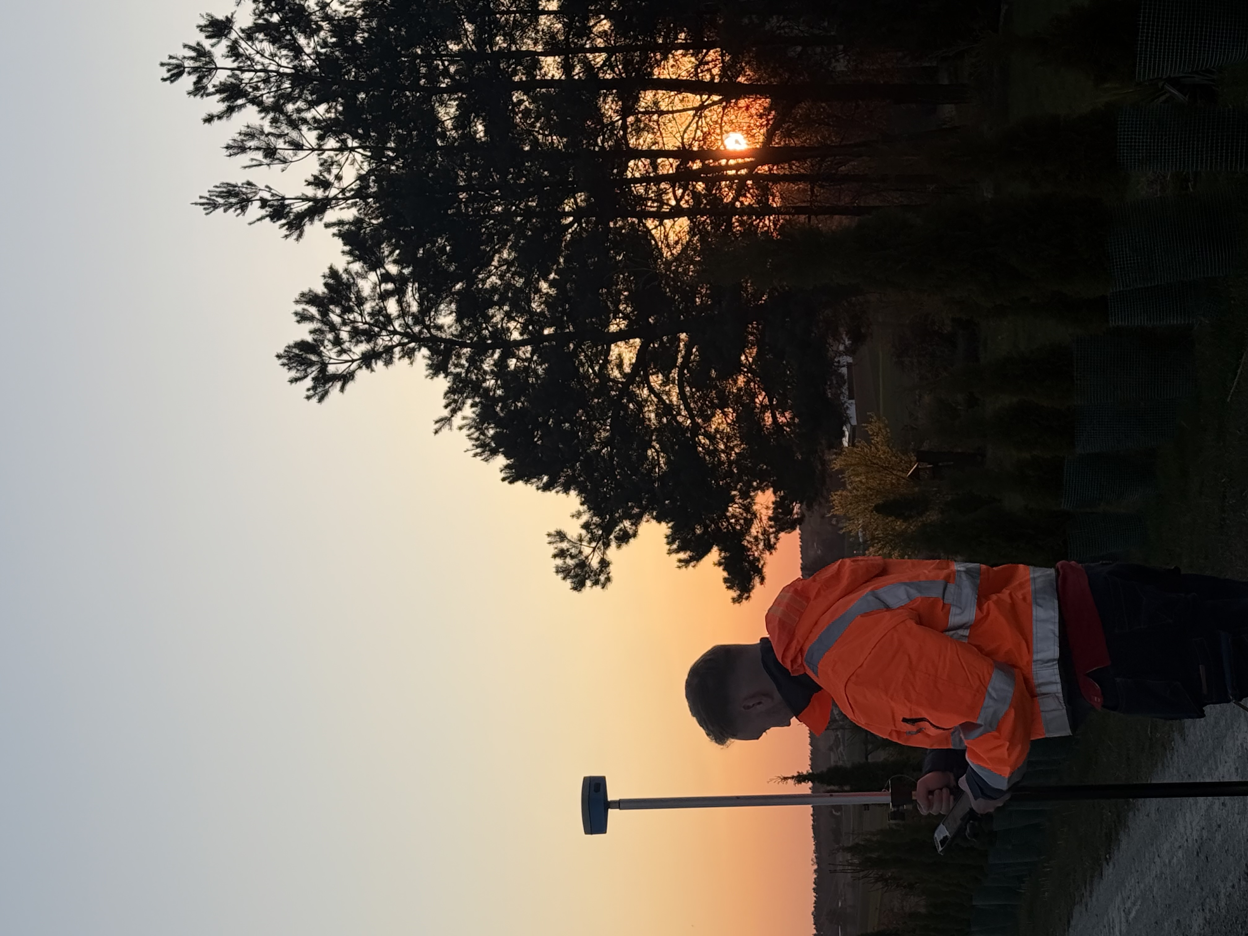 Geodeta z odbiornikiem GPS podczas pomiaru terenowego o zachodzie słońca